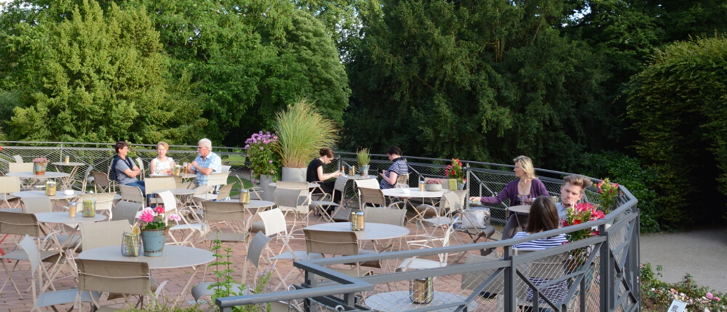 Dank Augusta Outdoor terrace with green natural surroundings. People are sitting at tables and talking.