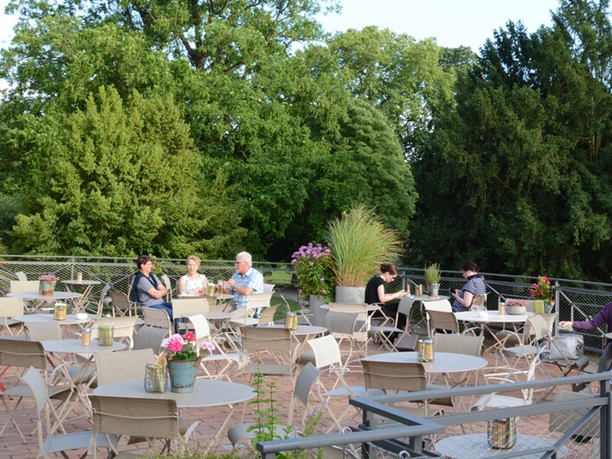 Dank Augusta Outdoor terrace with green natural surroundings. People are sitting at tables and talking.