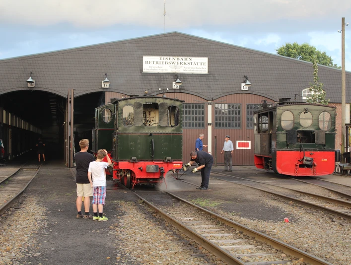 Hallen der Museums-Eisenbahn Bruchhausen-Vilsen Zwei historische Dampflokomotiven auf gleisüberdachtem Bahngelände, Menschen beobachten die Szene.