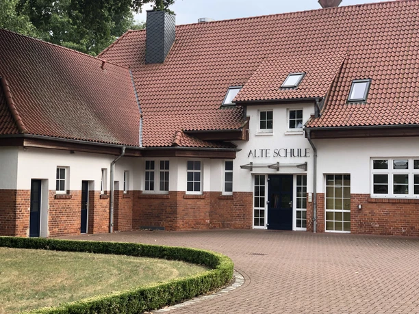 Alte Schule Rohrsen Ehemaliges Schulgebäude mit roten Ziegelwänden und Dachziegel, Büsche und gepflasteter Hof davor.