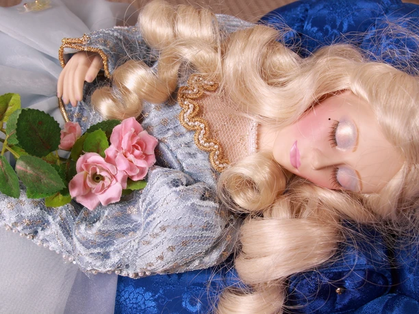 Puppenstube - Dornröschen Porzellanpuppe als Dornröschen in blau-goldenem Kleid mit Rosen in den Händen, friedlich schlafend.