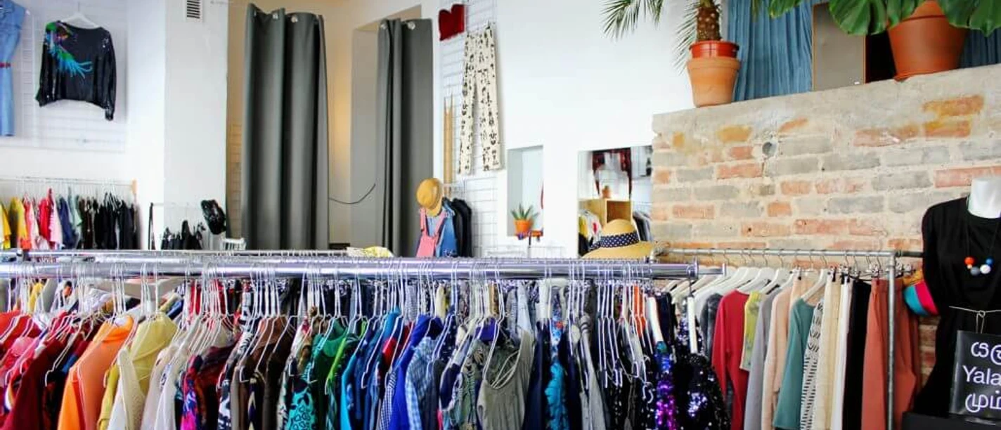 Kleiderei Innenansicht einer Boutique mit bunter Kleidung auf Kleiderständern und dekorativen Pflanzen.