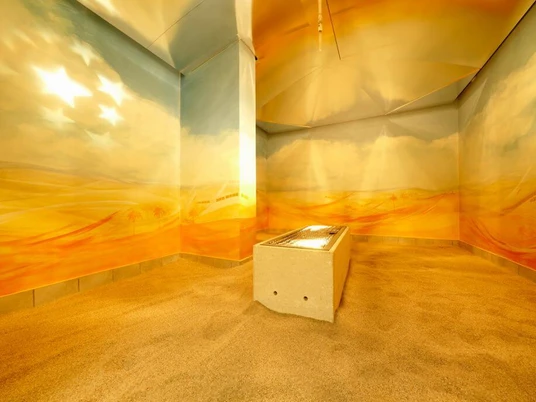 Agrippabad In einem warmen, sandfarbenen Raum steht eine beleuchtete Liege, umgeben von sanften Wandmalereien.An illuminated lounger stands in a warm, sand-colored room, surrounded by soft wall paintings.