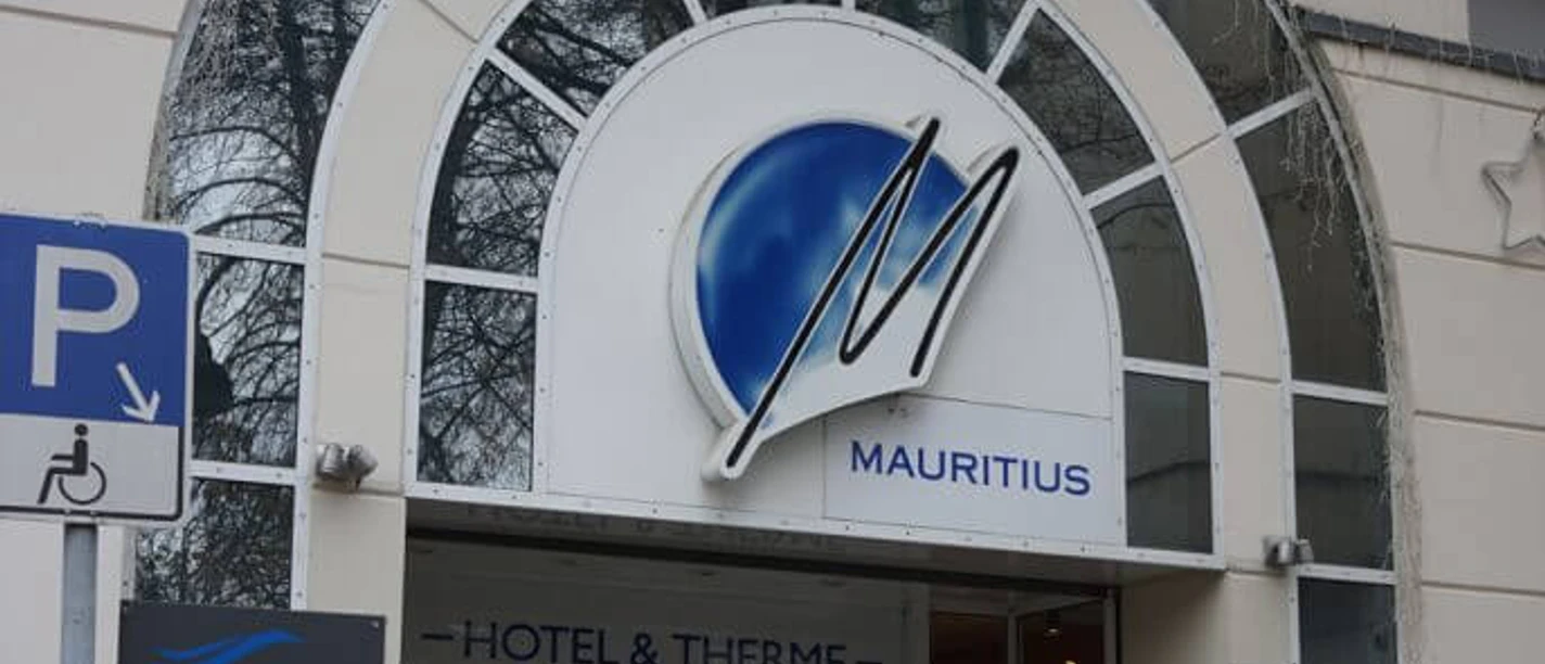 Mauritius Hotel und Therme Eingang zu Mauritius Hotel & Therme mit überdachtem Bogen und markantem blauen Logo.