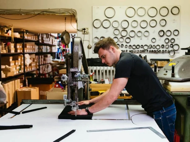 Hülden A young man works intently on an industrial machine, surrounded by shelves of metal parts.
