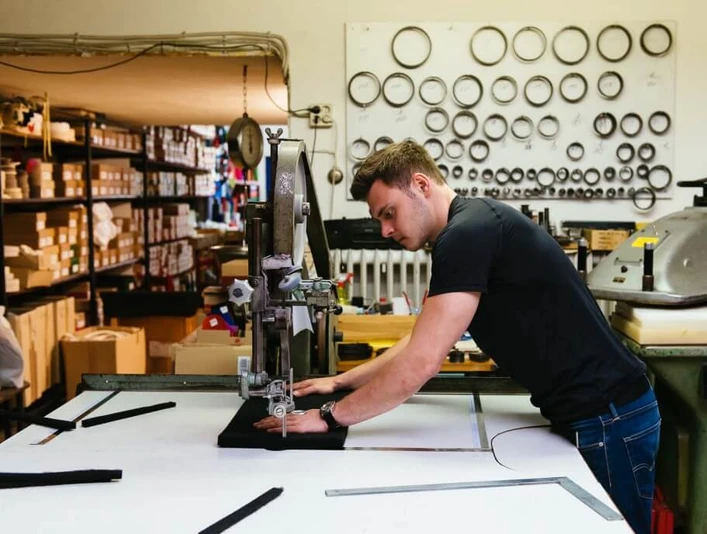 Hülden Ein junger Mann arbeitet konzentriert an einer Industriemaschine, umgeben von Regalen mit Metallteilen.A young man works intently on an industrial machine, surrounded by shelves of metal parts.