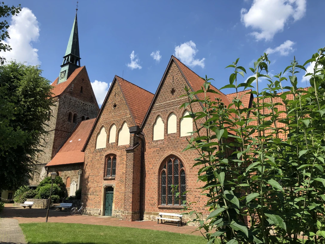 Backsteinkirche in sommerlicher Umgebung mit Fachwerkelementen und einem markanten Kirchturm.