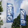 Zwei blaue Flaggen mit dem Logo und Schriftzug "VILSA Brunnen" wehen vor einem bewölkten Himmel.Two blue flags with the "VILSA Brunnen" logo and lettering fly in front of a cloudy sky.To blå flag med "VILSA Brunnen"-logo og -bogstaver vajer foran en overskyet himmel.Twee blauwe vlaggen met het logo en de letters "VILSA Brunnen" wapperen voor een bewolkte lucht.