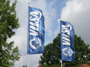 Vilsa Flaggen Zwei blaue Flaggen mit dem Logo und Schriftzug "VILSA Brunnen" wehen vor einem bewölkten Himmel.Two blue flags with the "VILSA Brunnen" logo and lettering fly in front of a cloudy sky.To blå flag med "VILSA Brunnen"-logo og -bogstaver vajer foran en overskyet himmel.Twee blauwe vlaggen met het logo en de letters "VILSA Brunnen" wapperen voor een bewolkte lucht.