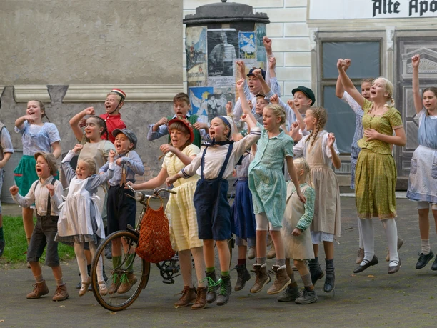 Eine Gruppe von Kindern in historischen Kostümen steht begeistert auf einer Freilichtbühne.