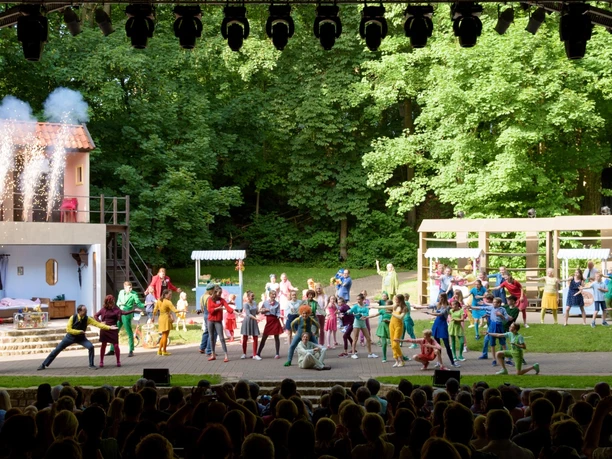 Freilichtbühne in Bökendorf Open-Air-Bühne mit farbenfroher Theateraufführung, umgeben von üppigem Grün und sichtbar begeistertem Publikum.