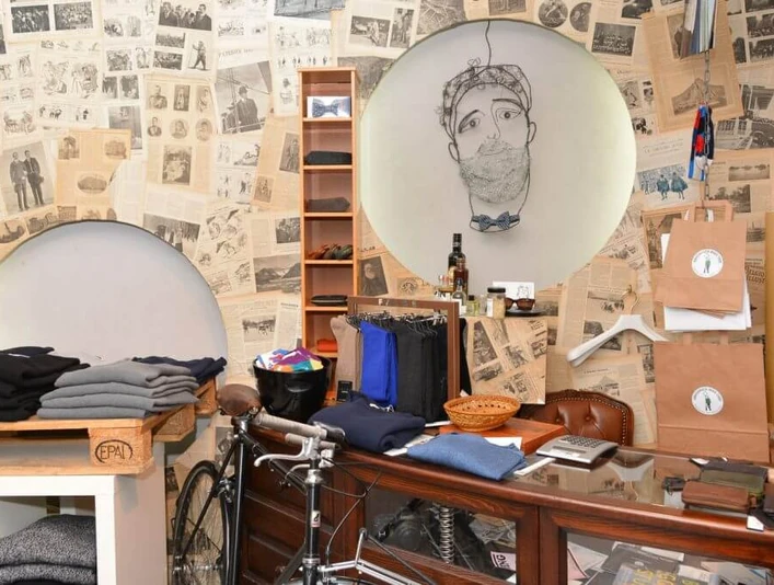 Greenwich Man Time Ein stilvoll eingerichteter Laden mit Vintage-Charme, dekoriert mit alten Zeitungen. Im Fokus stehen elegante Männerkleidung, Accessoires und ein Fahrrad. Ein gezeichnetes Porträt an der Wand. Modern und traditionell vereint.A stylishly furnished store with vintage charm, decorated with old newspapers. The focus is on elegant men's clothing, accessories and a bicycle. A painted portrait on the wall. Modern and traditional combined.