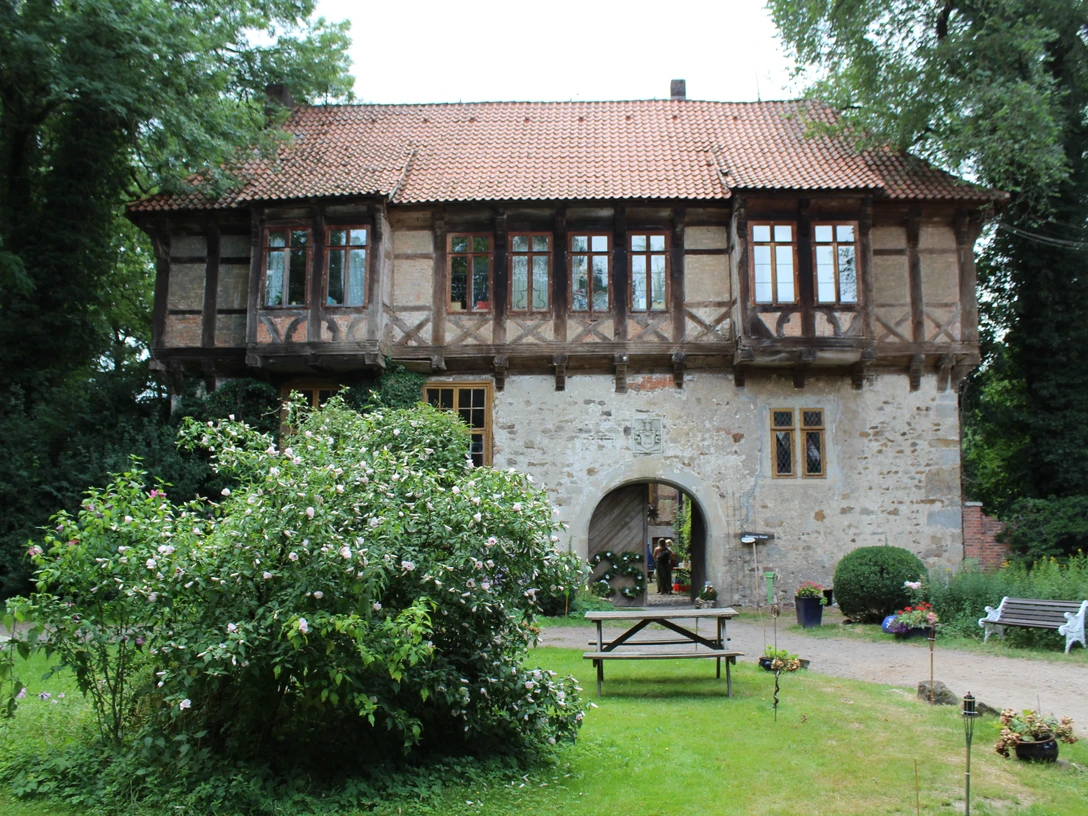 Historisches Gebäude mit Fachwerk, umgeben von Garten und kleiner Terrasse mit Bank und Tisch.