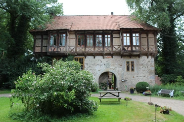 Rittergut Brokeloh Historisches Gebäude mit Fachwerk, umgeben von Garten und kleiner Terrasse mit Bank und Tisch.