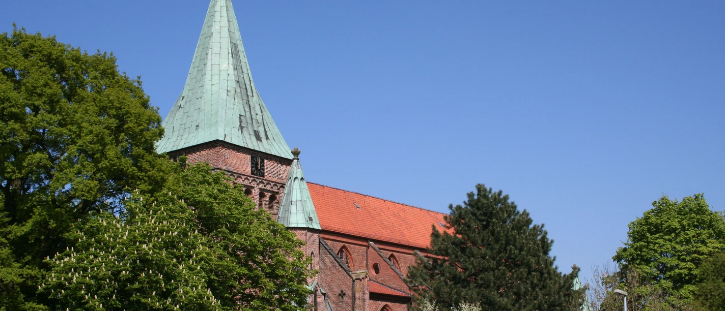 Red brick church with a green steeple roof, surrounded by green trees under a clear blue sky.