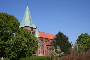 Felicianus Kirche Rote Backsteinkirche mit grünem Kirchturmdach, umgeben von grünen Bäumen unter klarem blauen Himmel.