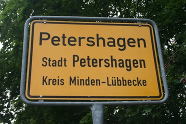 Ortsschild Petershagen Ortsschild der Stadt Petershagen im Kreis Minden-Lübbecke, umgeben von grünen Blättern.