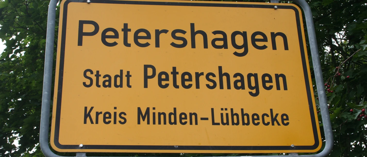Ortsschild Petershagen Ortsschild der Stadt Petershagen im Kreis Minden-Lübbecke, umgeben von grünen Blättern.