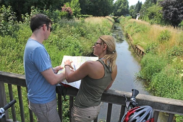 Radfahren Zwei Radfahrer stehen auf einer Brücke und betrachten eine Karte. Ein Fluss fließt darunter.