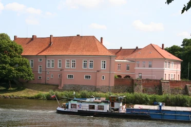 Old count's castle on the Weser, pink in color, surrounded by trees and river, in the calm daylight.