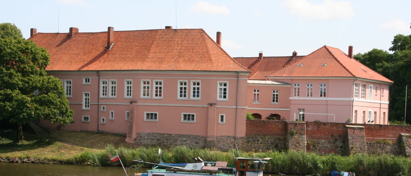 Old count's castle on the Weser, pink in color, surrounded by trees and river, in the calm daylight.