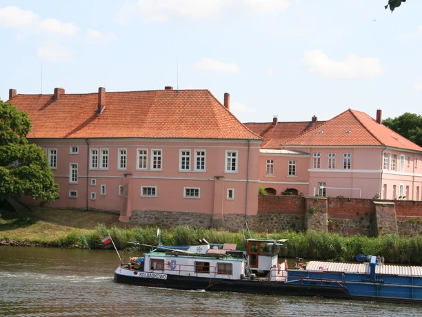 Old count's castle on the Weser, pink in color, surrounded by trees and river, in the calm daylight.