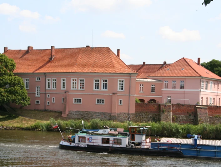 Grafenschloss zu Hoya Altes Grafenschloss an der Weser, rosafarben, umgeben von Bäumen und Fluss, im ruhigen Tageslicht.