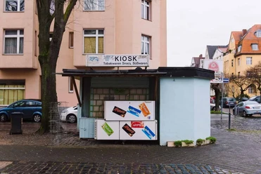 Kiosk at Nikolausplatz Small kiosk on a quiet street corner surrounded by residential buildings, featuring advertising boards for snacks.