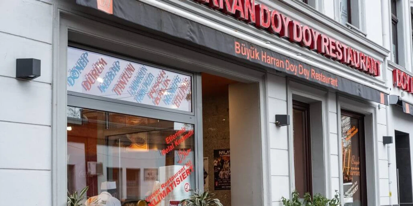Büyük Harran Doy Doy Außenansicht eines türkischen Restaurants mit großen Fenstern und Pflanzen am Eingang.Exterior view of a Turkish restaurant with large windows and plants at the entrance.