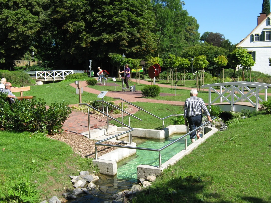 Eine Person nutzt das Wassertretbecken im Kurpark Bad Holzhausen bei sonnigem Wetter.