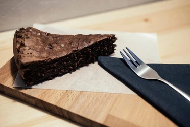 Cafe Einbrand A piece of chocolate cake on a wooden board with a fork.
