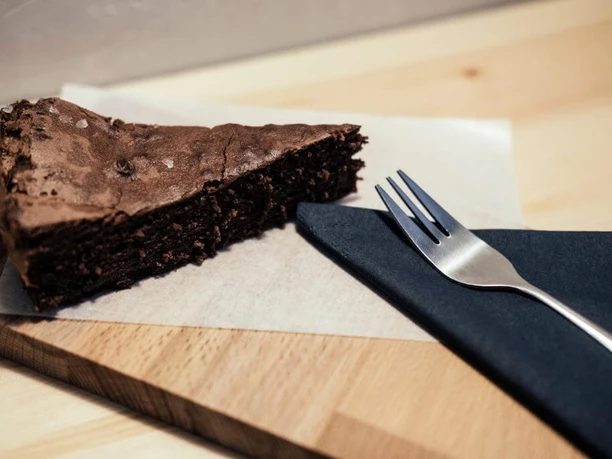 Cafe Einbrand Ein Stück Schokoladenkuchen auf Holzbrett mit Gabel.