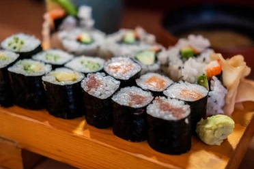 Momotaro Sushigerichte auf einem Holzbrett, inklusive Maki mit Lachs, Avocado und Gurke, kunstvoll arrangiert.