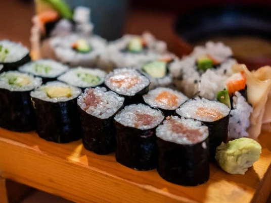 Momotaro Sushigerichte auf einem Holzbrett, inklusive Maki mit Lachs, Avocado und Gurke, kunstvoll arrangiert.Sushi dishes on a wooden board, including maki with salmon, avocado and cucumber, artfully arranged.