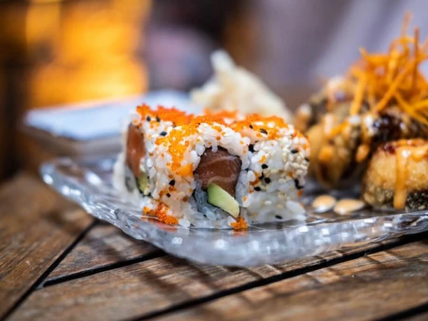 Tanoshii Sushi roll with salmon, avocado, and sesame seeds served on an elegant glass plate.
