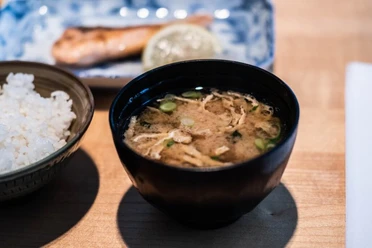 Restaurant Kintaro Nahaufnahme einer kleinen schwarzen Schüssel, gefüllt mit einer Rindersuppe, daneben ein Schälchen Reis.