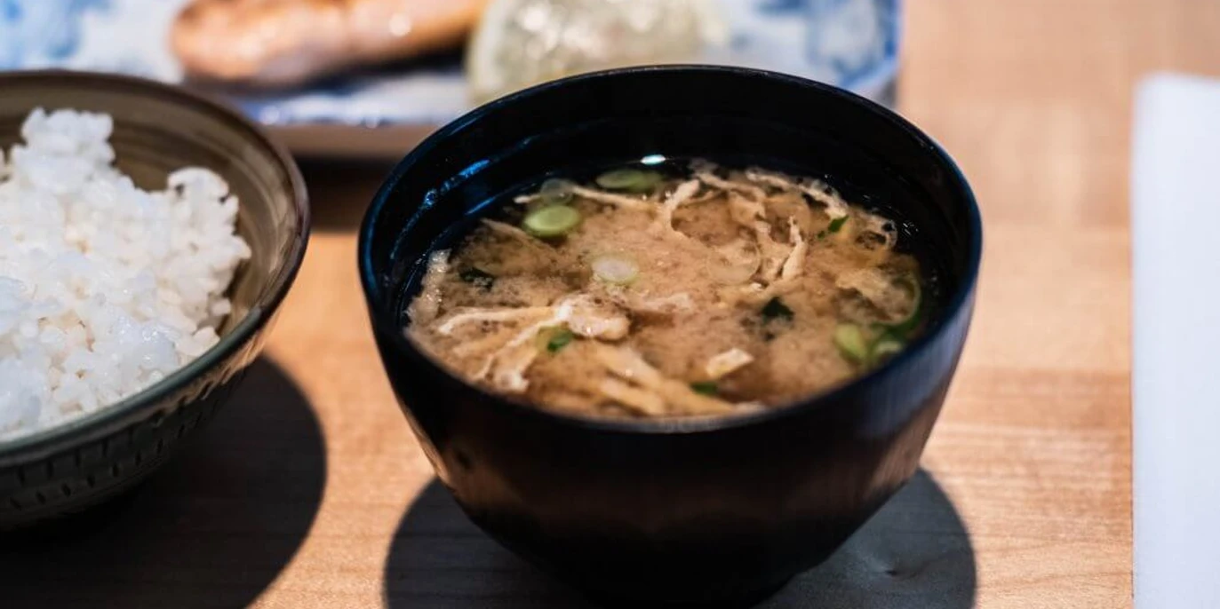 Restaurant Kintaro Nahaufnahme einer kleinen schwarzen Schüssel, gefüllt mit einer Rindersuppe, daneben ein Schälchen Reis. Close-up of a small black bowl filled with beef soup, next to it a small bowl of rice.