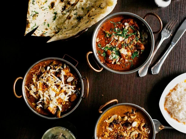 Ginti Ein Tisch gedeckt mit indischen Spezialitäten in kleinen Schüsseln dazu Reis und Naanbrot.