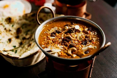 Ginti Nahaufnahme einer kleinen Metallschüssel mit Curry und Brotkorb, gefüllt mit Naanbrot.