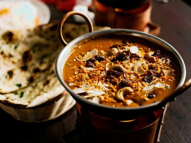 Ginti Nahaufnahme einer kleinen Metallschüssel mit Curry und Brotkorb, gefüllt mit Naanbrot.