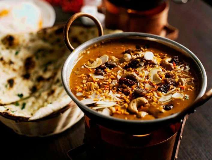 Ginti Nahaufnahme einer kleinen Metallschüssel mit Curry und Brotkorb, gefüllt mit Naanbrot.Close-up of a small metal bowl of curry and a bread basket filled with naan bread.