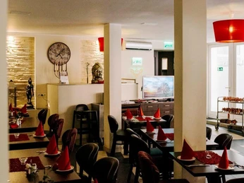 Ginti Innenansicht vom Restaurant mit dunklen Möbeln, hellen Wänden und roten Servietten. Interior view of the restaurant with dark furniture, light walls and red napkins.