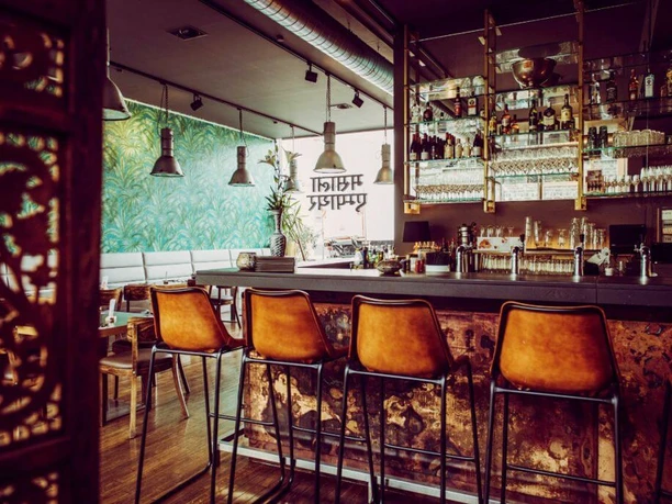 Masala Empire Ein stilvoll eingerichteter Barbereich mit einer langen Theke, Lederhockern und stilvoller Wanddekoration.