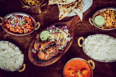 Masala Empire A magnificently laid Indian festive table with rice, curry, naan bread and juicy tandoori chicken legs.