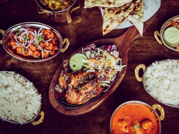 Masala Empire Ein prachtvoll angerichteter indischer Festtisch mit Reis, Curry, Naan-Brot und saftigen Tandoori-Hähnchenschenkeln.