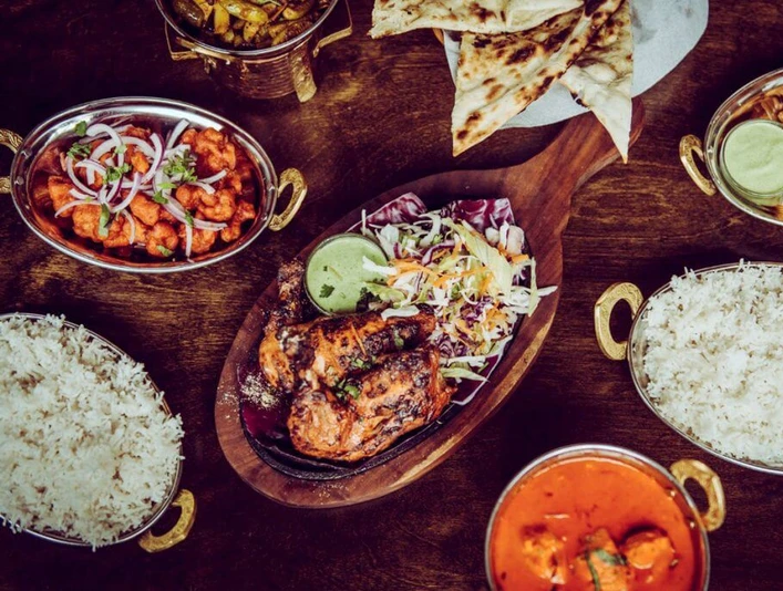 Masala Empire Ein prachtvoll angerichteter indischer Festtisch mit Reis, Curry, Naan-Brot und saftigen Tandoori-Hähnchenschenkeln.A magnificently laid Indian festive table with rice, curry, naan bread and juicy tandoori chicken legs.