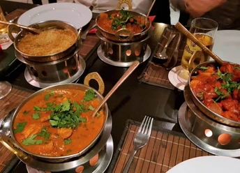 Royal Punjab Vier dampfende Curry-Gerichte in typischen indischen Servierschalen auf einem gedeckten Tisch.