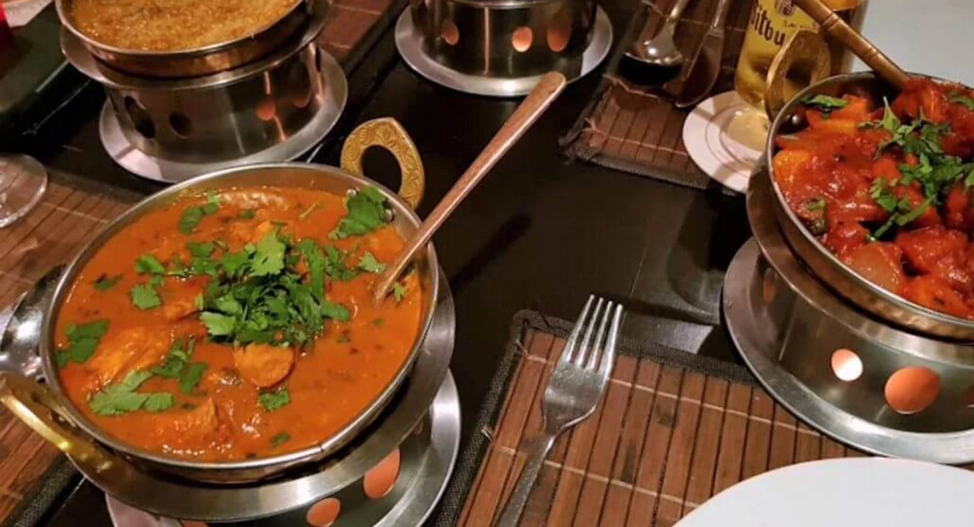 Royal Punjab Vier dampfende Curry-Gerichte in typischen indischen Servierschalen auf einem gedeckten Tisch.Four steaming curry dishes served in traditional Indian bowls, arranged on a set table.