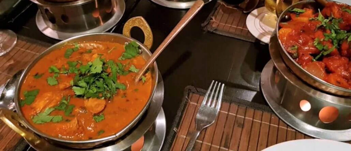 Royal Punjab Vier dampfende Curry-Gerichte in typischen indischen Servierschalen auf einem gedeckten Tisch.