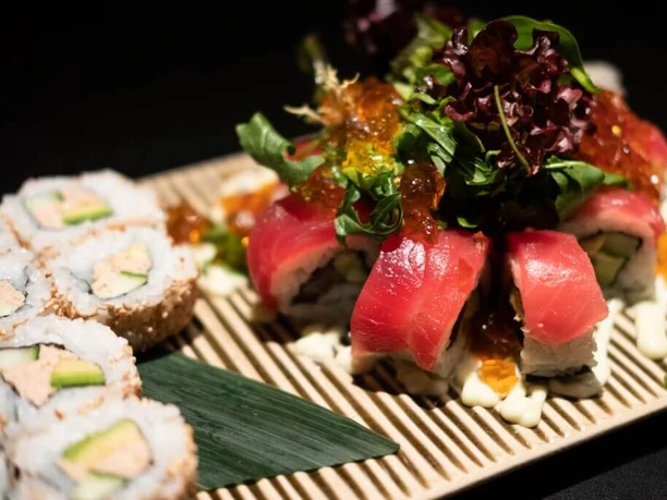 Zen Eine Auswahl an Sushi, darunter Nigiri und Maki, sorgfältig auf einem Bambusbrett arrangiert.